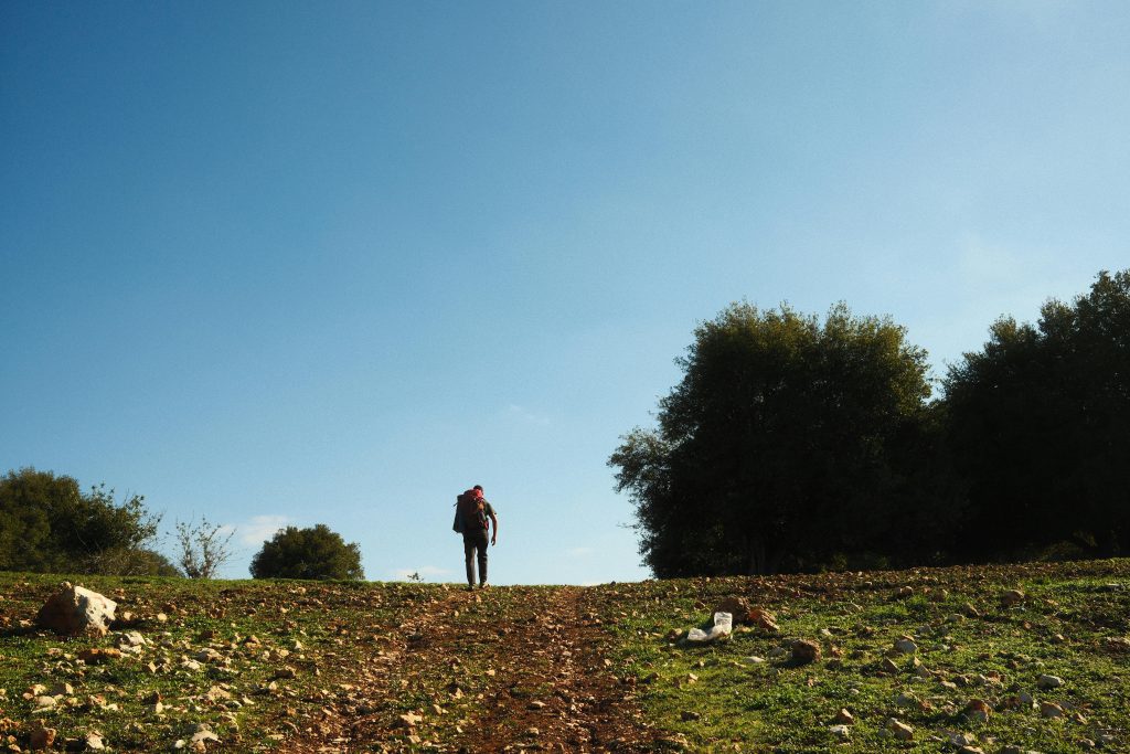 Lone hiker walking uphill in a scenic, rural landscape under a clear blue sky.